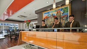 A reception area with a wooden counter, a painting, and a view of the outside. - M Citi Suites (Cebu City)