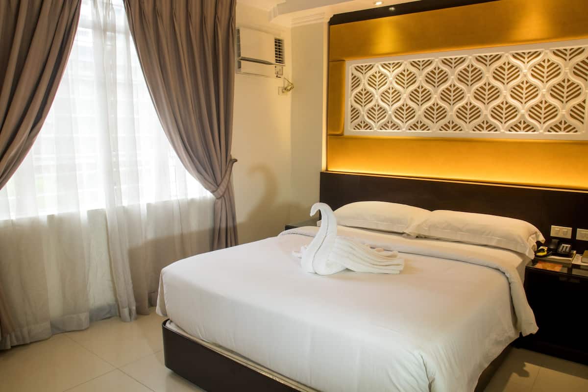 A hotel room with a bed, curtains, a wall-mounted air conditioner, a decorative panel, and a bedside table with a phone.
