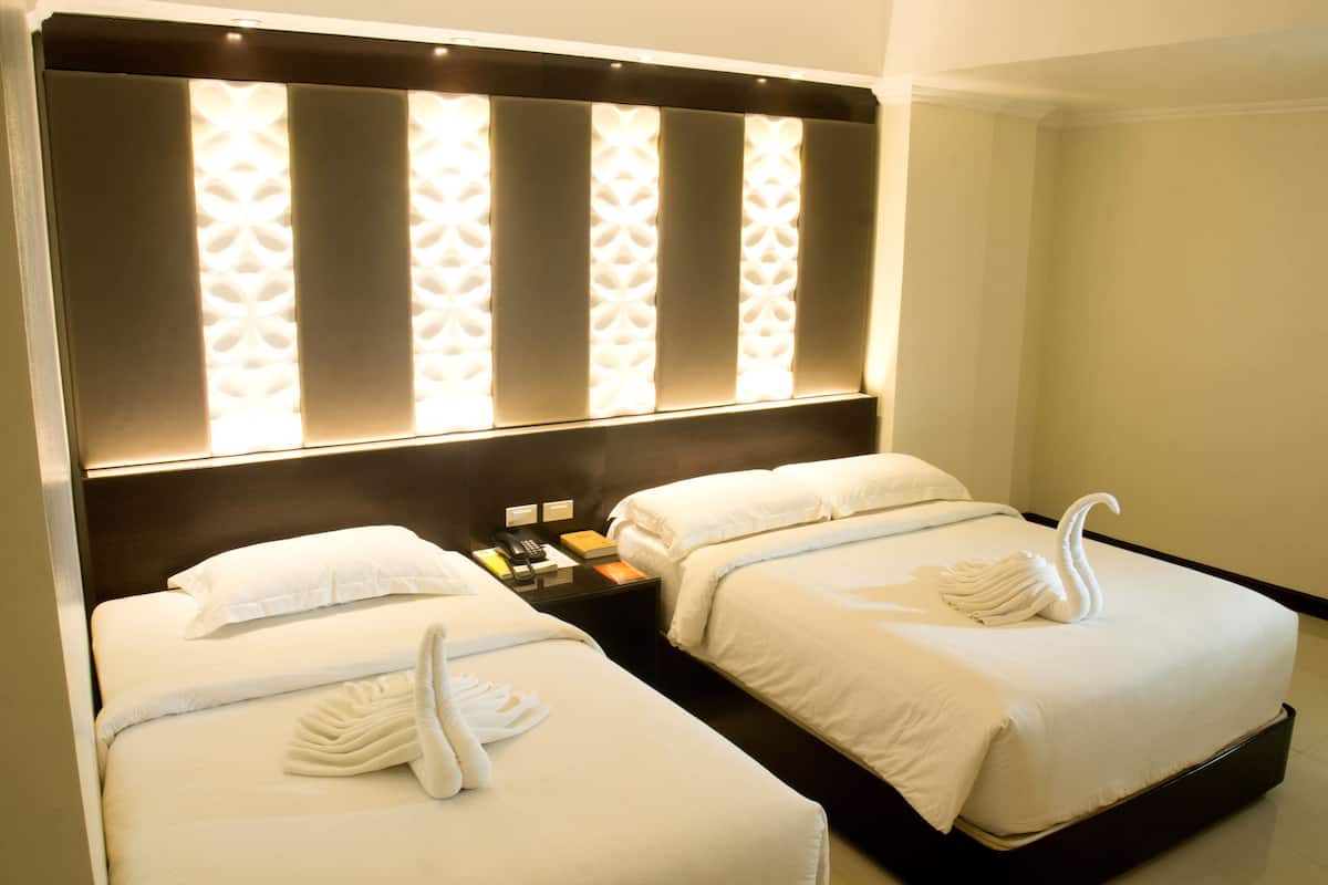 A hotel room with two beds, each with a swan towel and a bedside phone.