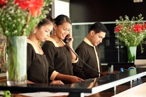 A reception desk with a glass partition, vases with flowers, and a telephone. - M Citi Suites (Cebu City)
