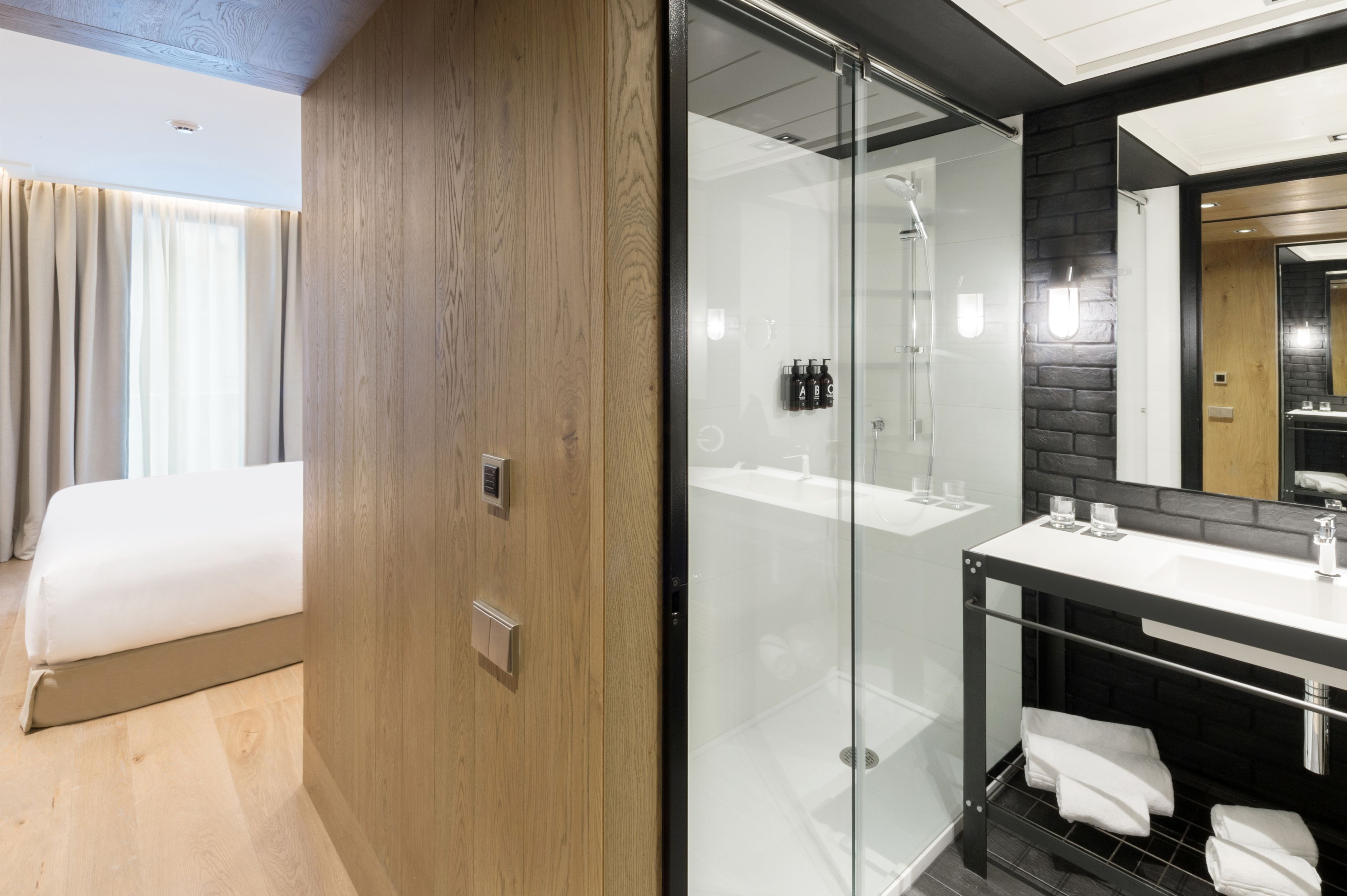 Une chambre d’hôtel moderne comprenant un lit, une douche en verre, une coiffeuse avec un miroir et un mur d’accent en bois.