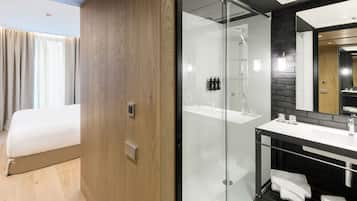 Une chambre d’hôtel moderne comprenant un lit, une douche en verre, une coiffeuse avec un miroir et un mur d’accent en bois.