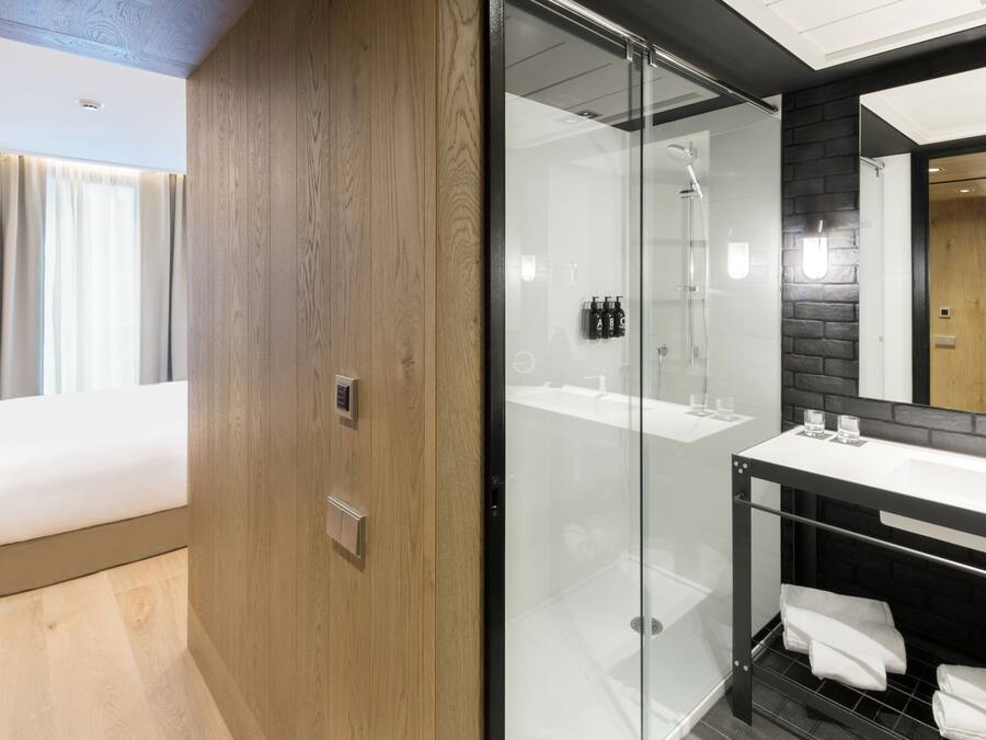 Une chambre d’hôtel moderne comprenant un lit, une douche en verre, une coiffeuse avec un miroir et un mur d’accent en bois.