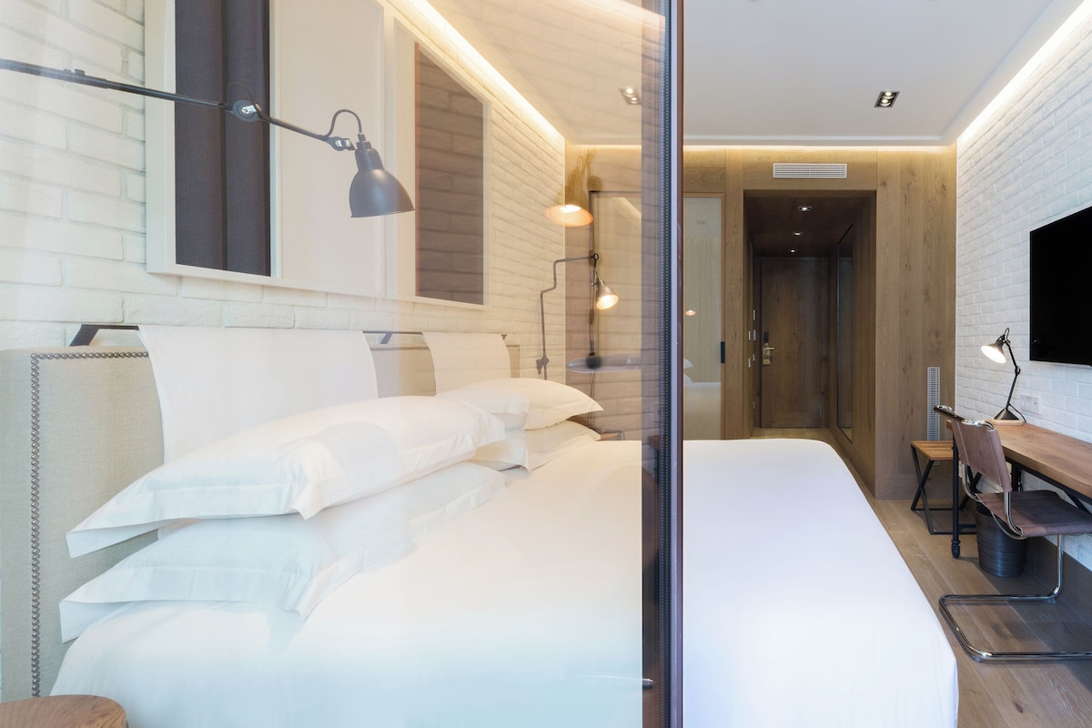 Une chambre d’hôtel moderne équipée d’un lit, d’un bureau et d’une chaise, d’un téléviseur et d’une cloison en verre.