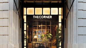 The entrance to The Corner Hotel with a black awning, a glass door, and a visible interior with a lamp and plants. - The Corner Hotel (Barcelona)
