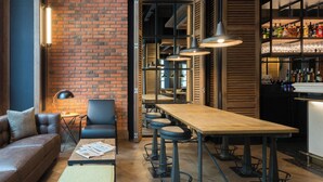 A modern bar area with a brick wall, wooden shelves, and a long wooden table with bar stools. - The Corner Hotel (Barcelona)
