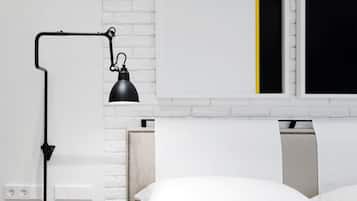 A modern room with a white brick wall, a black desk lamp, a bed with white bedding, and a window with a yellow stripe.