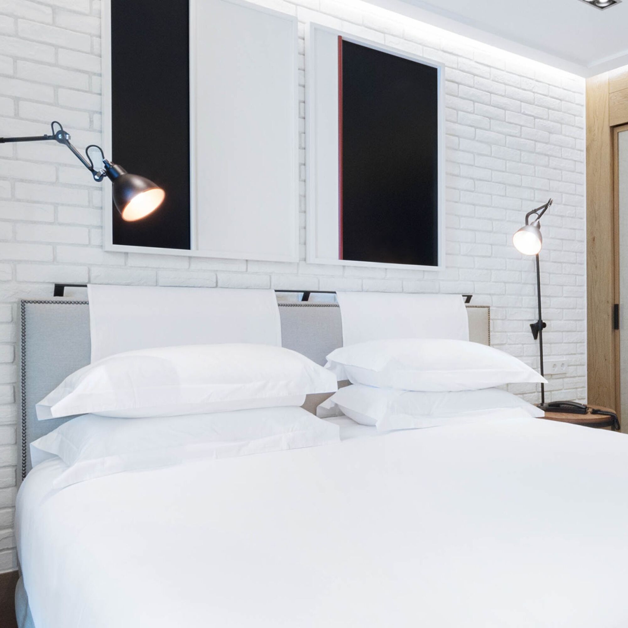 A modern bedroom with a white brick wall, a bed with white bedding, and two wall-mounted lamps.