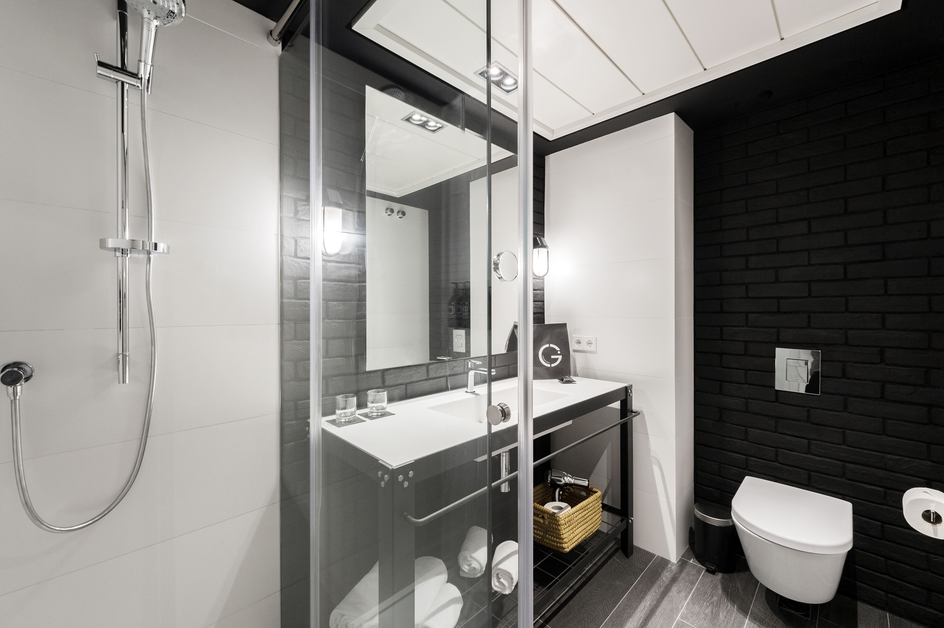 Un bagno moderno con doccia vetro, lavandino bianco e parete in mattoni neri.