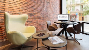 Un hall d’hôtel moderne avec un mur en briques, une grande fenêtre donnant sur la rue et un mobilier contemporain comprenant un fauteuil jaune, une chaise marron et une table ronde avec un ordinateur portable.