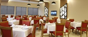 A restaurant with multiple tables and chairs, each set with white tablecloths and red chairs. - Fayton Hotel (Akhisar)