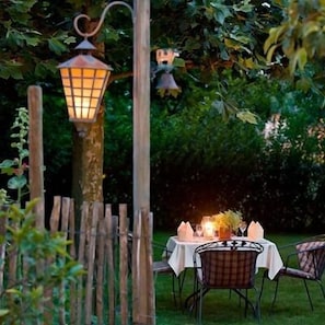 Un espace extérieur aménagé pour les repas, avec une table dressée pour deux personnes, entouré d’une clôture en bois et agrémenté d’un lampadaire.