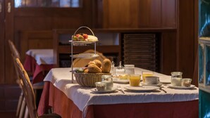 Une table dressée pour le petit-déjeuner, avec un présentoir à trois niveaux où sont disposés des fruits et du pain, un panier de viennoiseries et divers autres éléments pour le petit-déjeuner.