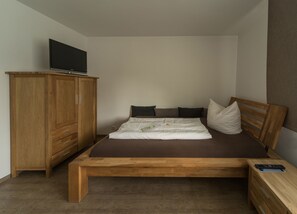 Une chambre à coucher avec un lit en bois, un téléviseur posé sur un meuble, une armoire en bois et une table de chevet avec une télécommande.