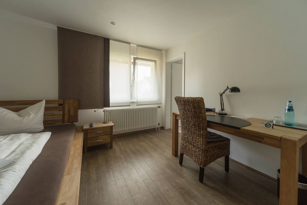Un dormitorio con cama, escritorio, silla, radiador y ventana.