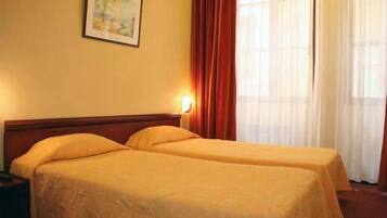 A hotel room with two single beds, a nightstand, a framed picture on the wall, and a window with curtains.