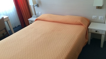 Una habitación de hotel con una cama, dos mesitas de noche, una lámpara y un escritorio.