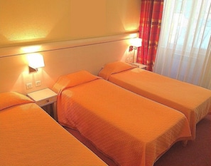 A hotel room with three single beds, each with an orange bedspread. There are bedside lamps and a nightstand with a lamp on it. The room has a window with red curtains. - Hôtel Elysée (Lyon)
