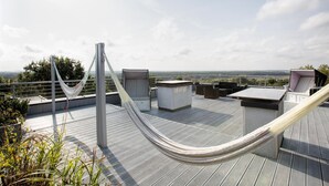 Eine Dachterrasse mit Hängematte, Gartenmöbeln und Blick auf die Landschaft.