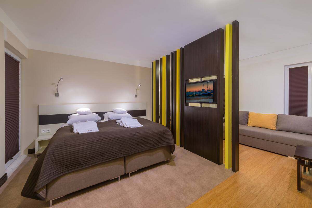 Una habitación de hotel moderna con una cama grande, un sofá y un televisor montado en un panel de madera.