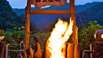 A stone archway with a sign, a fire pit, and a mountainous landscape in the background.