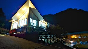 A modern building with large windows and a sloped roof, surrounded by trees and a small outdoor seating area. - Hsinchu Bali Forest Hot Spring Resort (Jianshi)