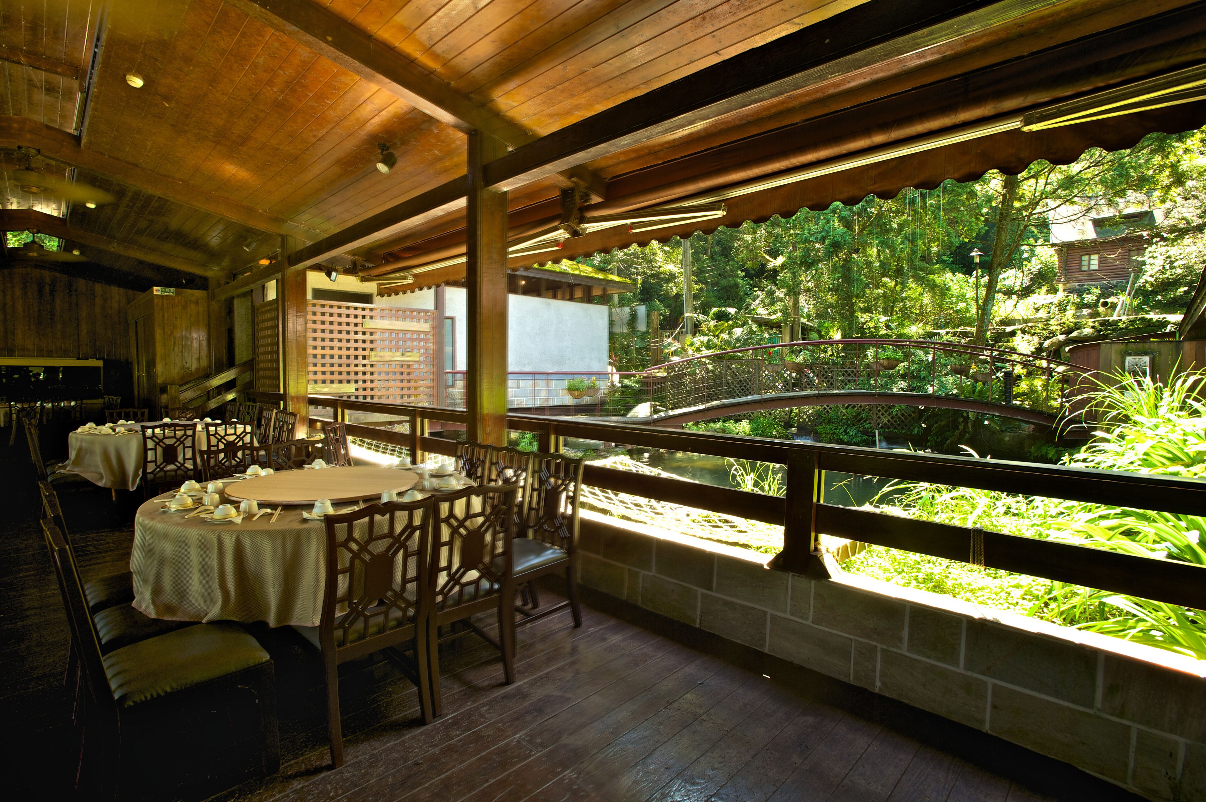 Un restaurante con mesas y sillas de madera, una pared de piedra y vistas al verdor.