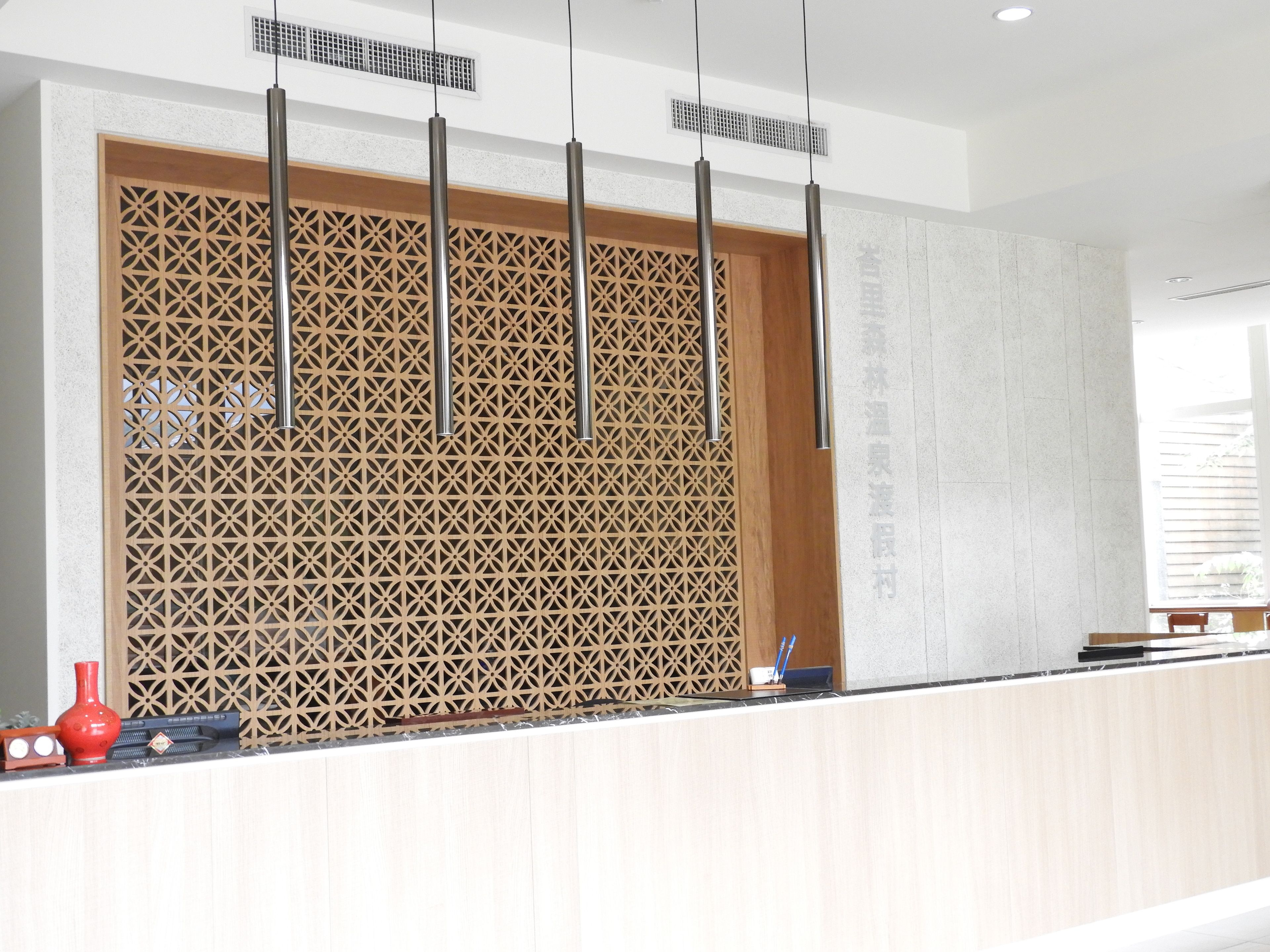 A reception area with a wooden decorative panel, a counter with a vase, and pendant lights.