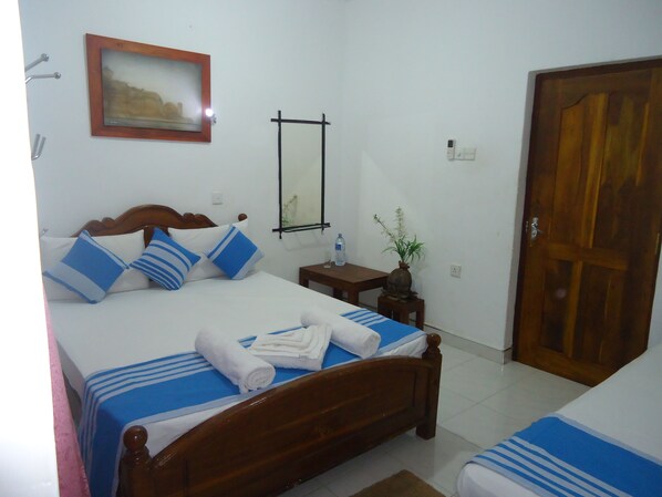 A hotel room with a wooden bed, a bedside table with a vase, a mirror, and a wooden door.