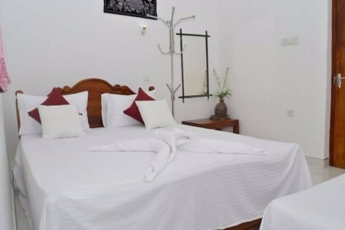 A neatly made bed with white bedding and a wooden headboard, a bedside table with a vase of flowers, and a coat rack against the wall.