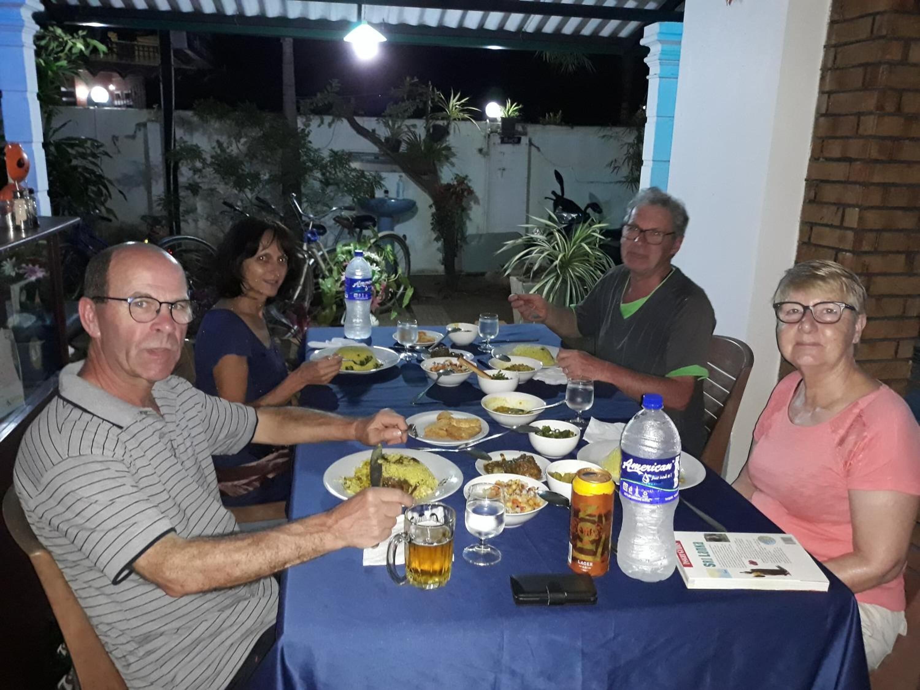 A group of people dining at an outdoor table with various dishes and drinks.