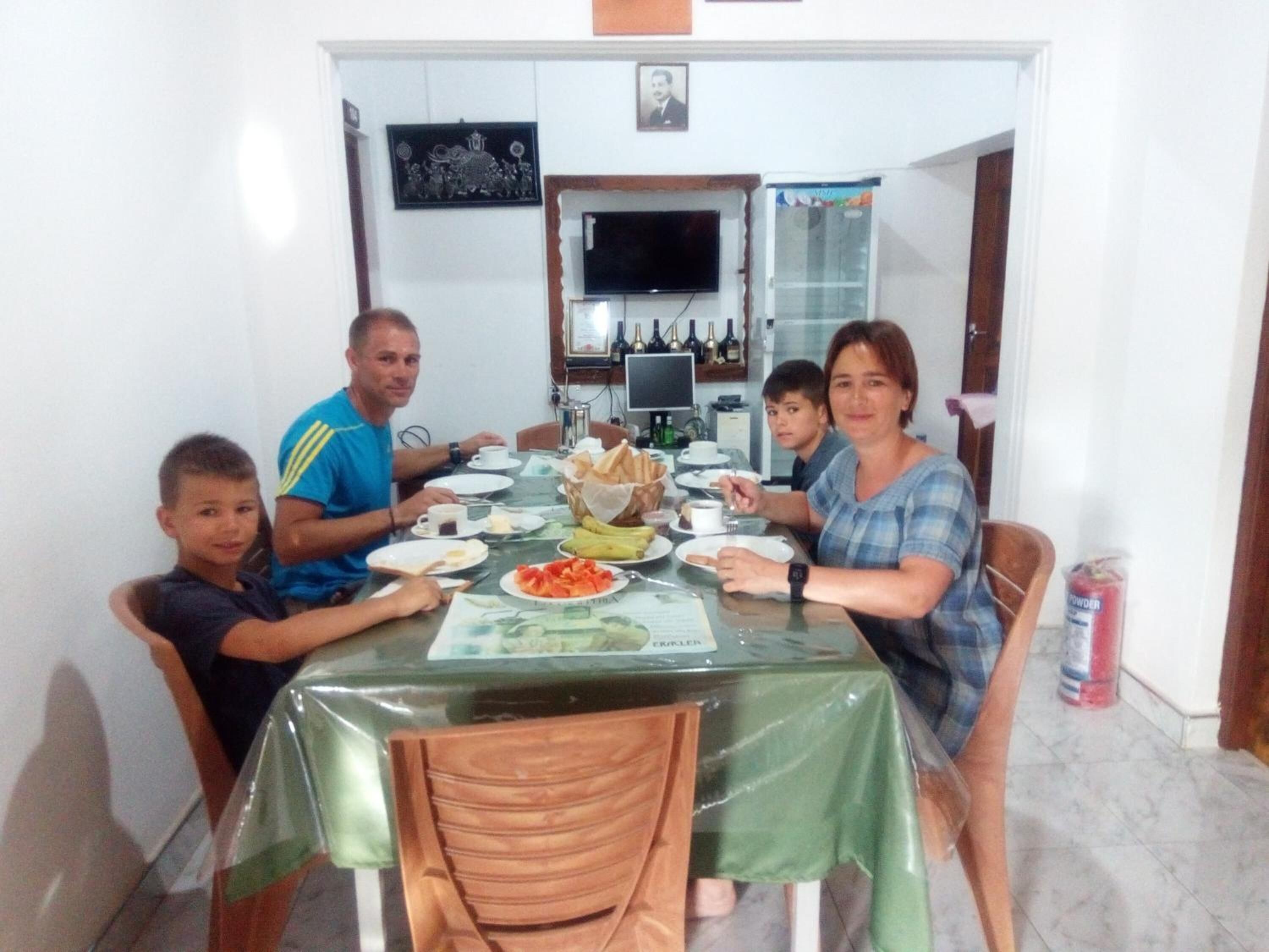 A family dining at a table with a green tablecloth, surrounded by chairs.