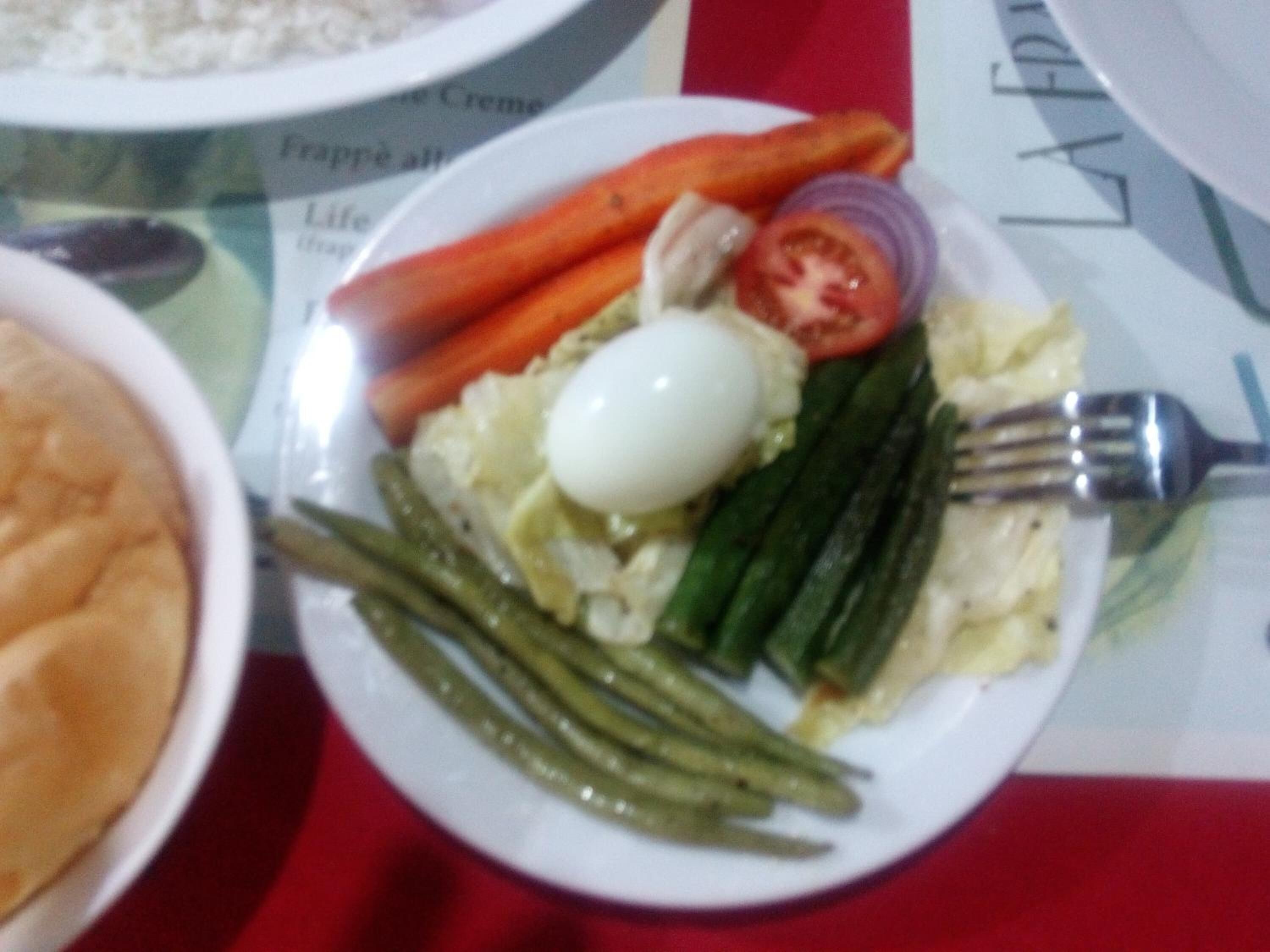 A plate with vegetables and an egg on a table with a red tablecloth.