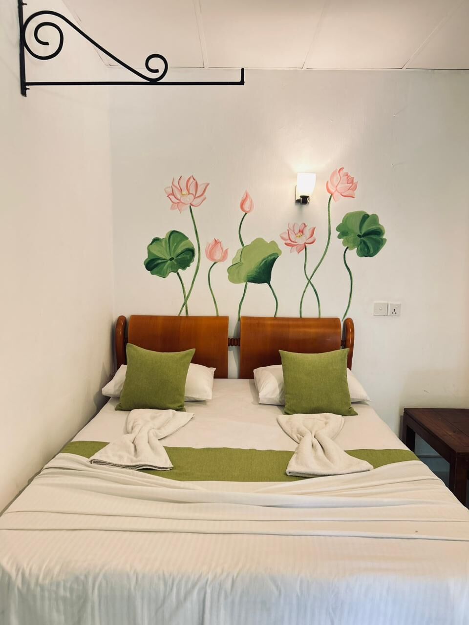 Une chambre d’hôtel avec un lit, deux oreillers, une lampe fixée au mur et un mur décoratif orné de motifs de fleurs de lotus.