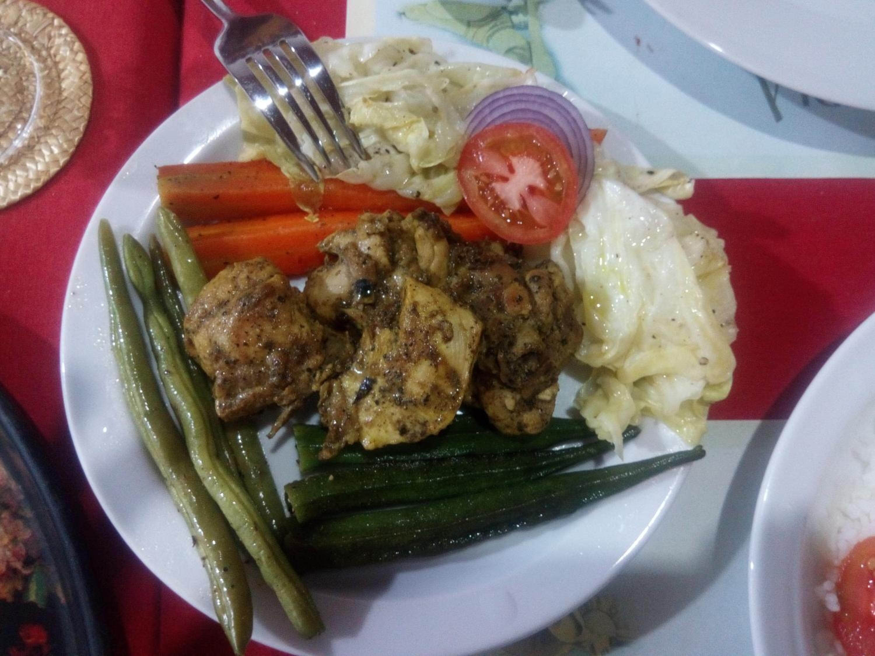 A plate with grilled chicken, green beans, carrots, cabbage, and a slice of tomato.