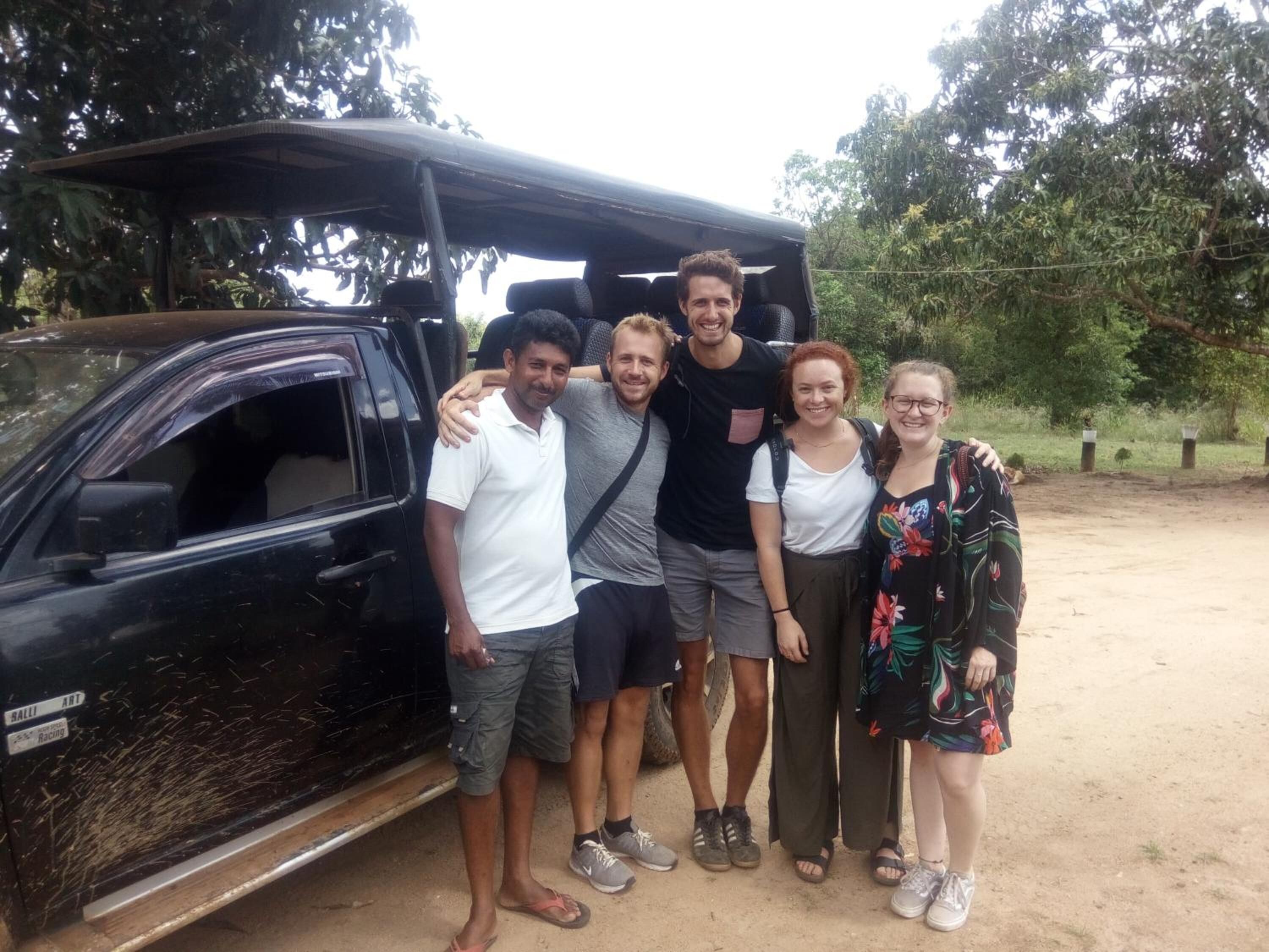 A group of people standing in front of a black SUV with an open roof.