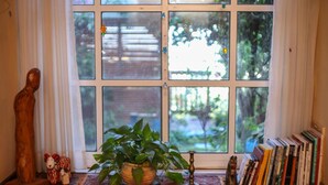 A window with a view of greenery, a wooden shelf with books, a potted plant, and a small figurine. - Havaya Ba Nof (Rosh Pinna)