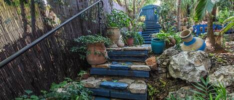 Un jardín con escalones de piedra, plantas en macetas y una valla de bambú.