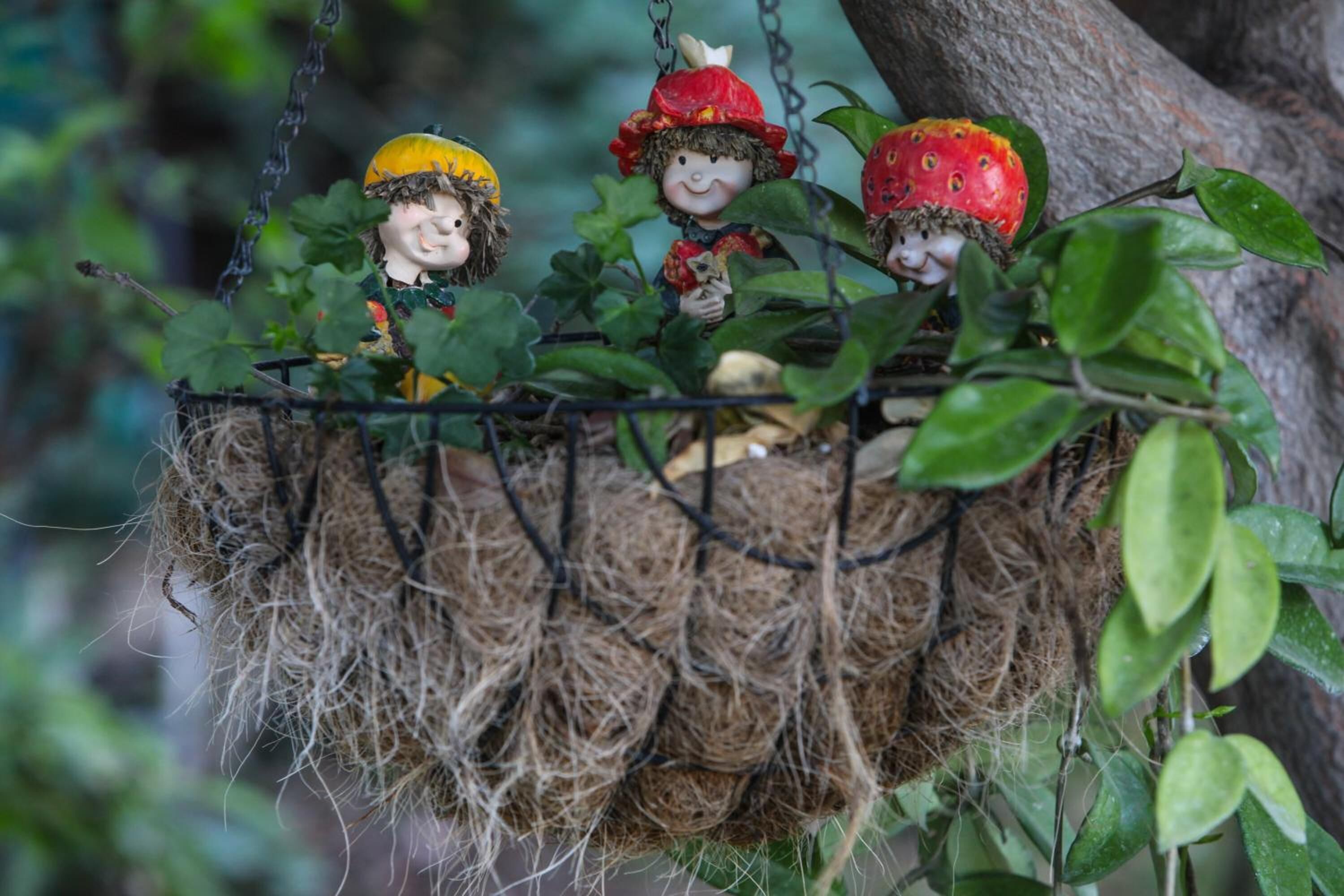 A decorative hanging with three figurines, each wearing a hat and holding a fruit.