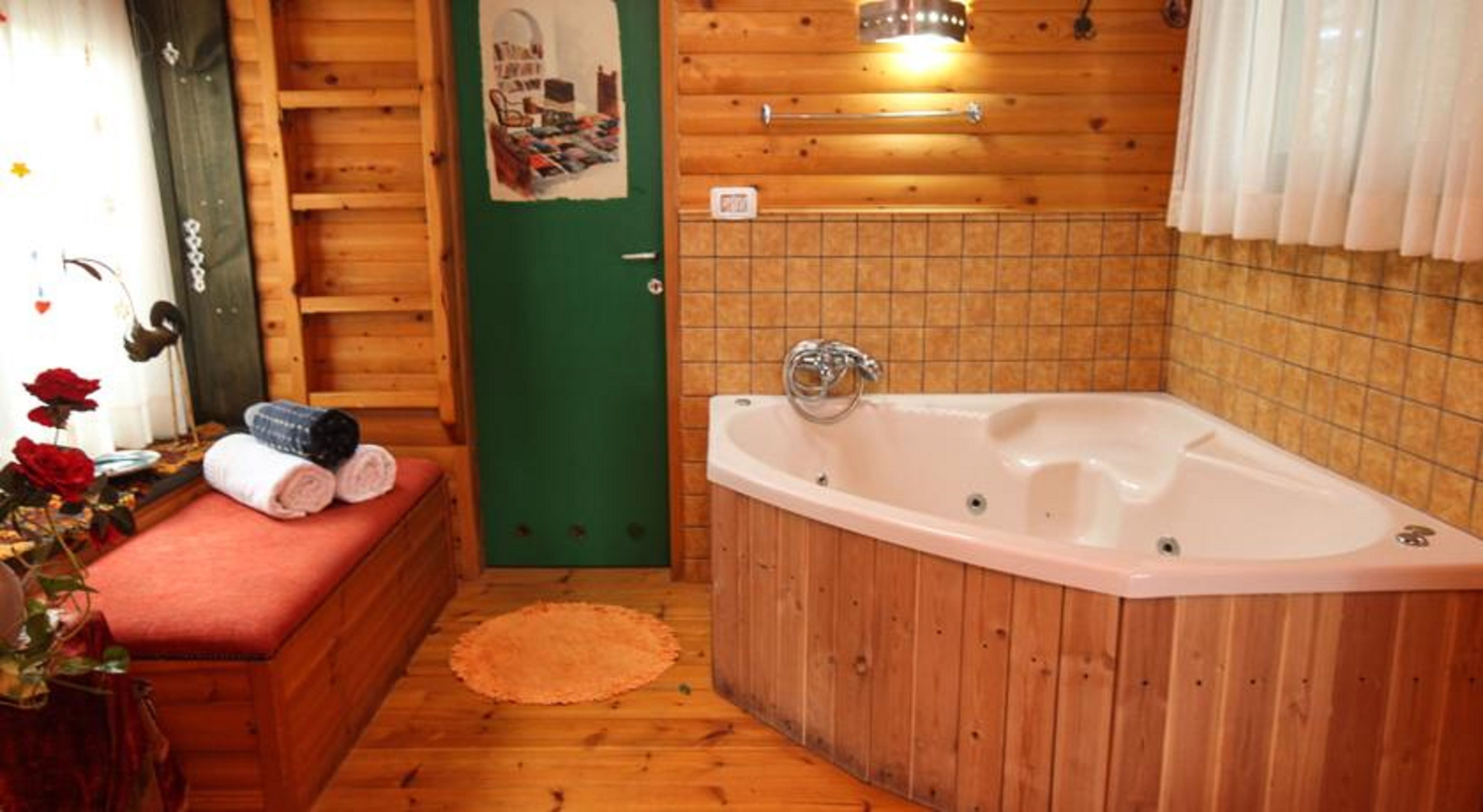 Une cabane en bois avec une grande baignoire, un banc avec des serviettes et une porte verte.