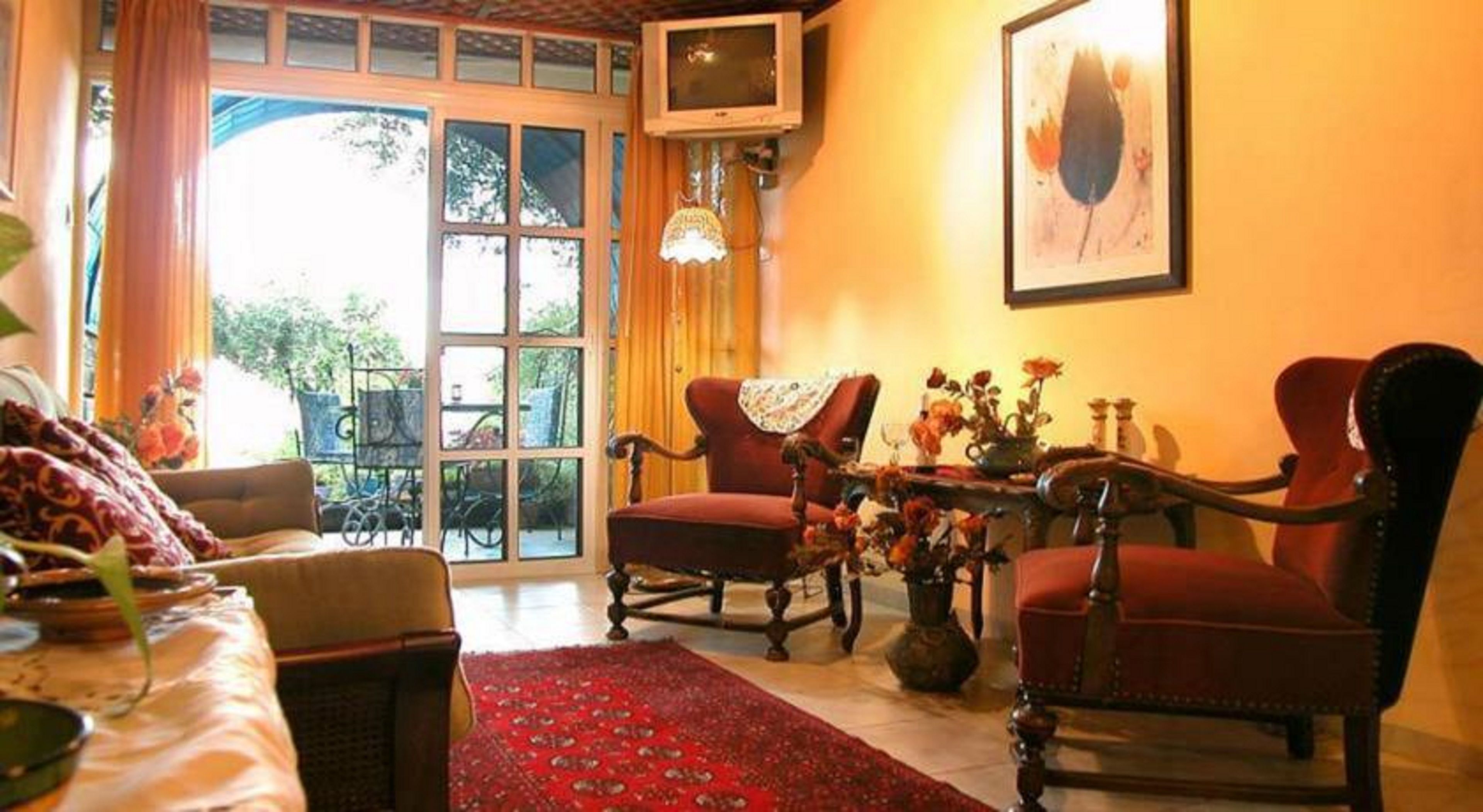 A cozy living room with a red armchair, a sofa, and a television on a wall.