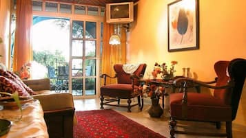 A cozy living room with a red armchair, a sofa, and a television on a wall.