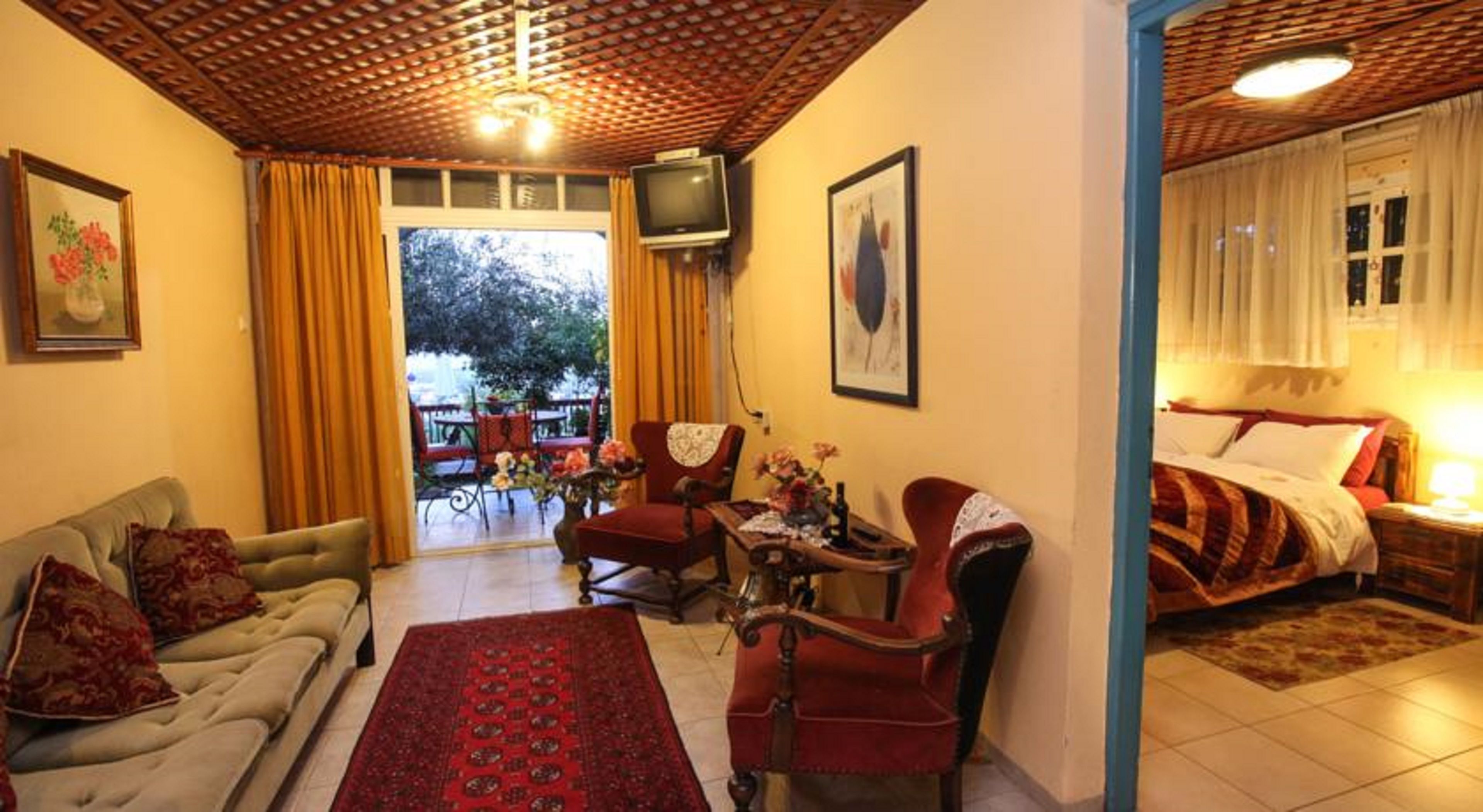 Ein gemütliches Wohnzimmer mit einer Couch, Sesseln, einem Couchtisch und einem Fernseher. Ein Balkon mit Tisch und Stühlen befindet sich im Freien.
