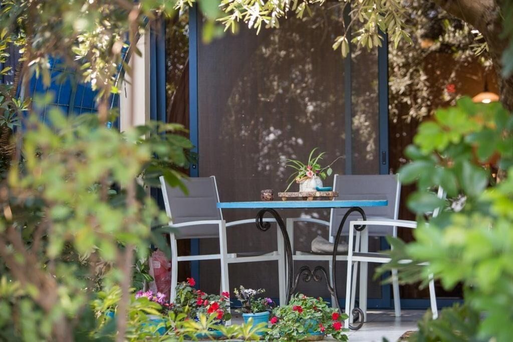 Un patio al aire libre con una mesa y sillas, rodeado de macetas con plantas y flores.