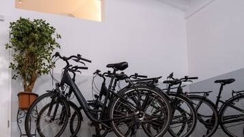 A row of bicycles parked against a wall with a potted plant beside them.