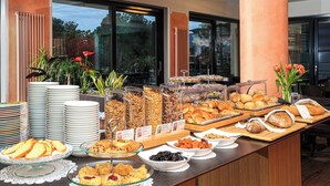 Un bufé con diversas opciones de comida, como pasteles, frutas y sándwiches, dispuesto sobre una mesa de madera con vistas al exterior a través de amplios ventanales.
