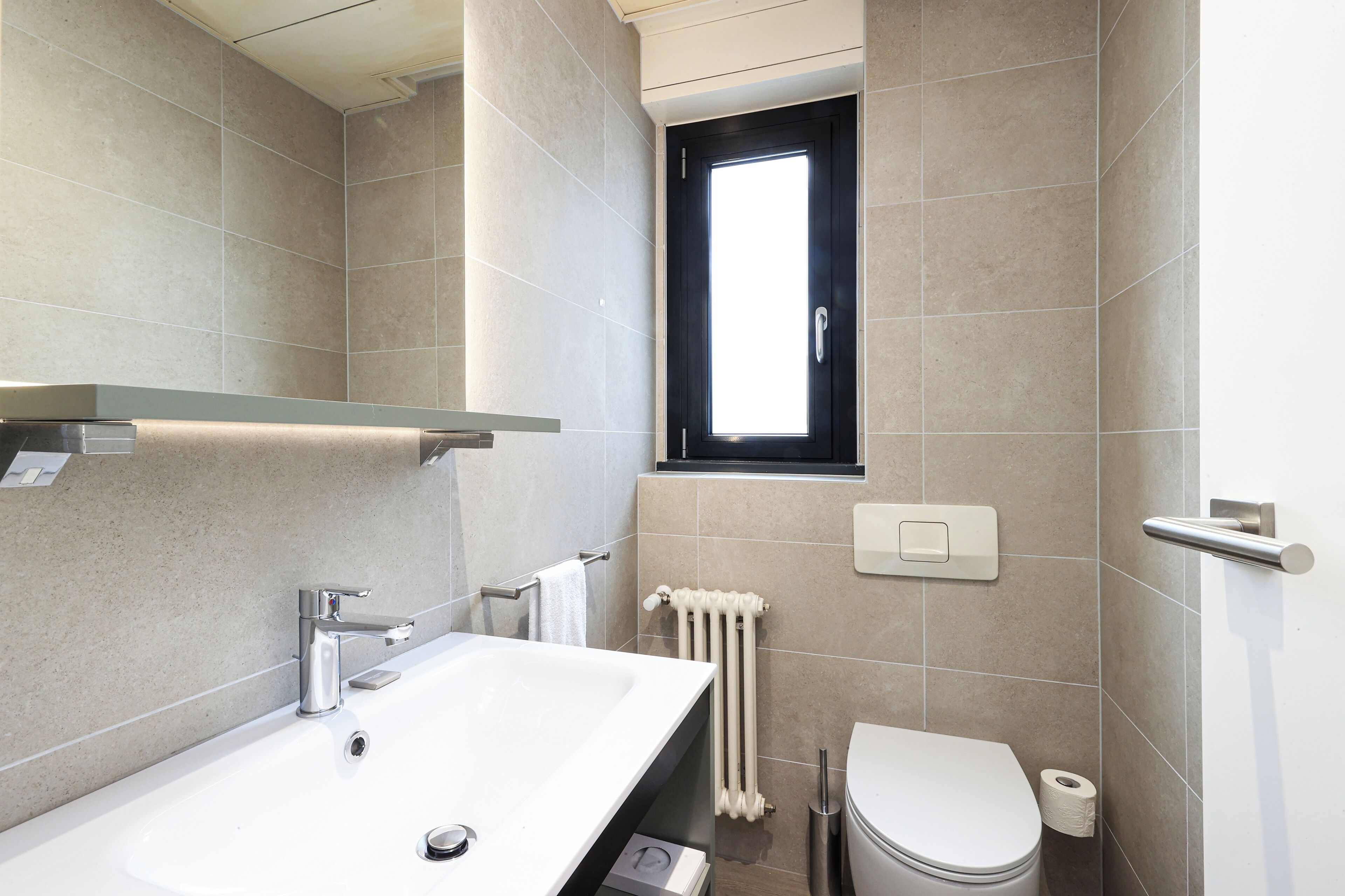 A modern bathroom with a white sink, a toilet, and a window above the toilet.