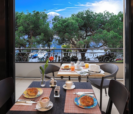 A dining area with tables set for breakfast, overlooking a scenic view of trees and a body of water.