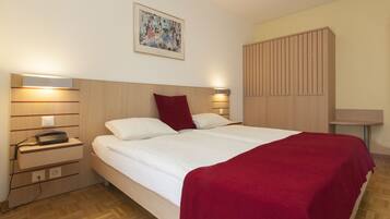 A neatly made bed with a red blanket, a bedside lamp, a telephone, and a wall-mounted artwork.