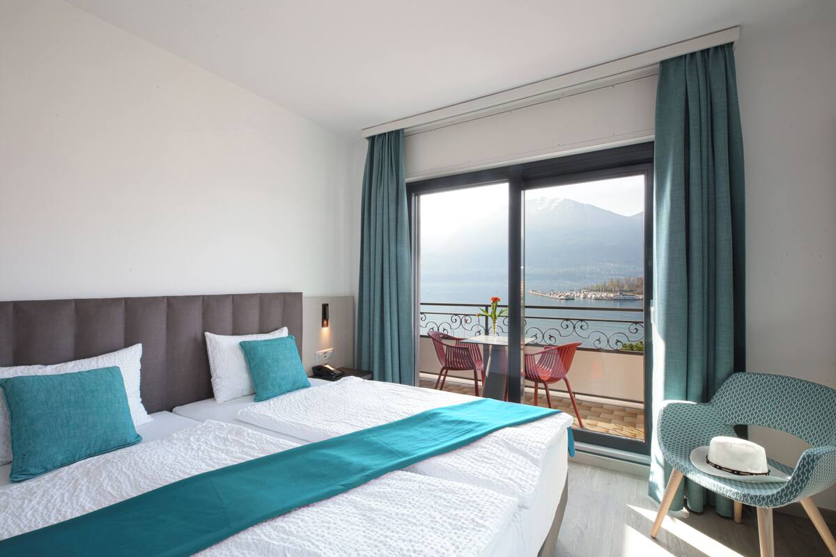 Una habitación de hotel con una cama grande, un balcón con vistas y una silla con sombrero.